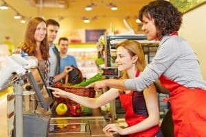 In-store sales associates work with cashiers at the grocery checkout to help waiting customers with their purchases.